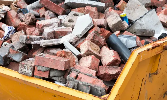 Cumulo di mattoni rotti e detriti edili in un cassone giallo. Questo è il materiale di risulta, scarti di demolizione pronti per lo smaltimento.