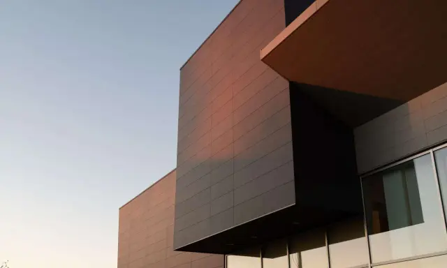 Edificio moderno con facciata ventilata in pannelli scuri e color rame, illuminato dalla luce del tramonto.