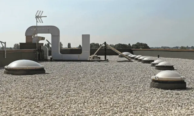 Tetto piano ricoperto di ghiaia, con lucernari a cupola e condotti di ventilazione. Il vespaio ghiaia protegge la copertura.