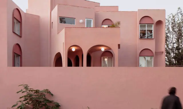 Edificio moderno con un particolare colore intonaco esterno rosa cipria. Archi e finestre a tutto sesto creano un gioco di luci e ombre.