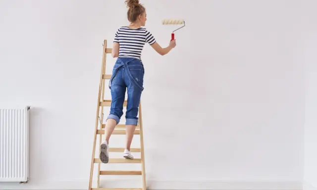 Donna su scala con rullo, pronta a tinteggiare le pareti di bianco.