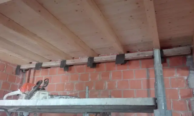 Travetti in legno per solaio, con staffe metalliche fissate a un muro di mattoni. L'interasse travetti solaio è visibile.