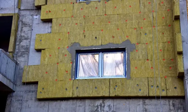 Iniziano i lavori per fare il cappotto alla casa: pannelli isolanti gialli fissati al muro grezzo, con finestre protette.
