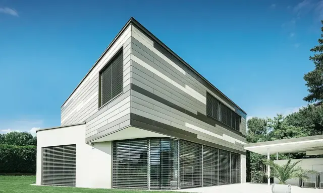 Moderna casa con pareti esterne a fasce grigie e bianche, grandi finestre con persiane e prato verde.