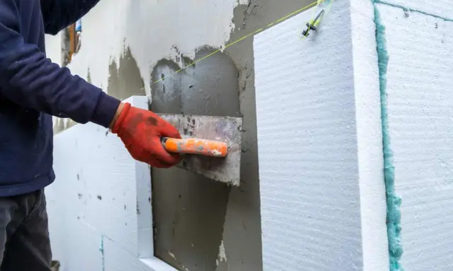Lavoratore applica intonaco su pannelli isolanti per creare una parete a cappotto.