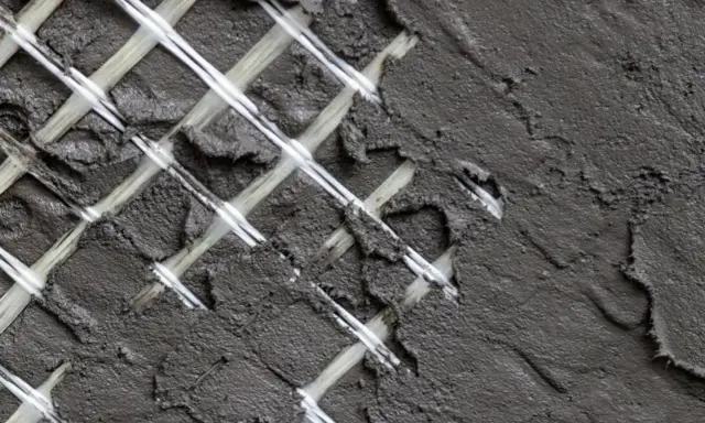 Rete in fibra di vetro coperta da malta grigia, un dettaglio di un intervento locale per rinforzare una superficie.