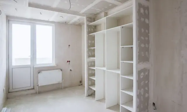 Un armadio bianco con ripiani è in fase di installazione. Sopra l'armadio, si intravede il cartongesso del soffitto, in attesa di finitura.
