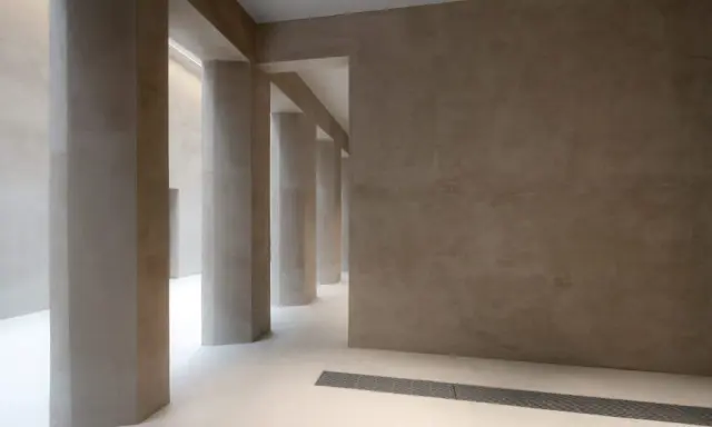 Colonnato moderno con pareti e pilastri in intonaco o stucco color sabbia, illuminato da luce soffusa.