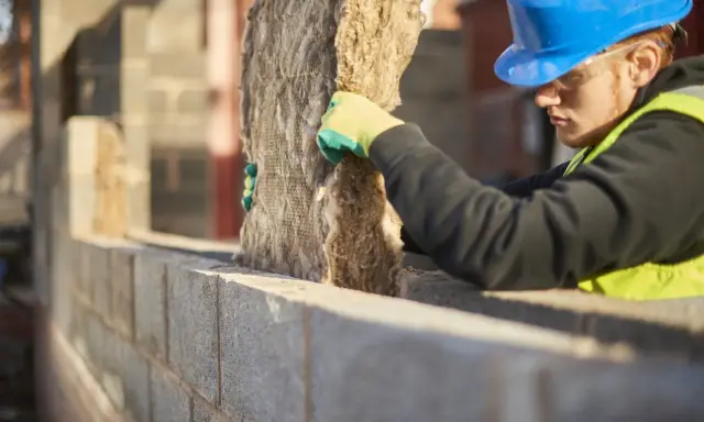 Operaio con casco blu installa isolante, valutando i cappotto termico svantaggi.