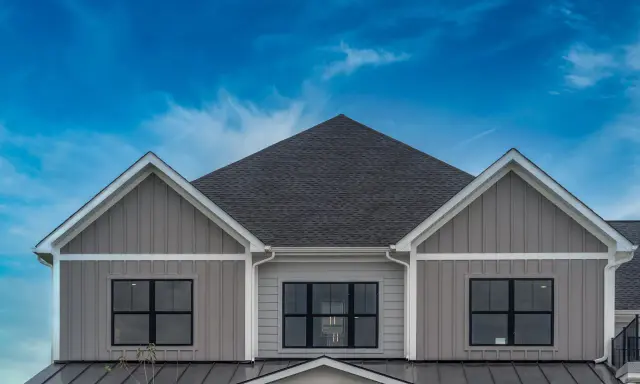 La facciata di una casa moderna con un elegante colore esterno casa tortora scuro, finestre nere e un tetto scuro sotto un cielo blu intenso.