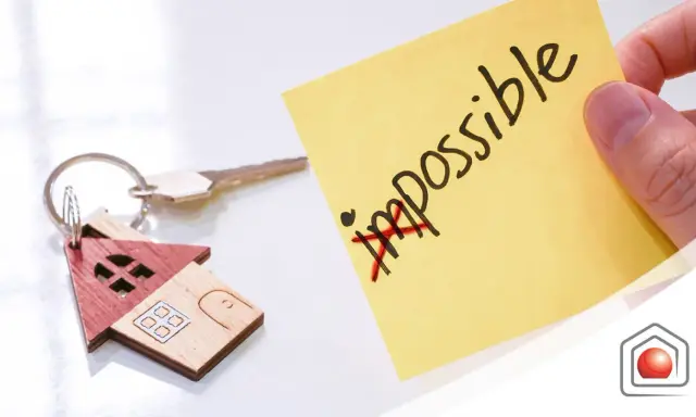 Chiavi di casa con portachiavi a forma di casetta. Post-it giallo con "impossible" barrato, simboleggia che l'edilizia convenzionata pro e contro può diventare possibile.