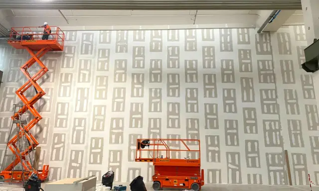 Lavori in corso su una parete con pannelli di cartongesso rei. Due piattaforme aeree arancioni sono posizionate per raggiungere l'altezza.