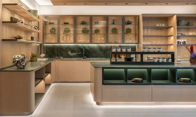 Una cucina moderna con un'isola centrale. Il piano di lavoro e il paraschizzi in marmo verde creano un contrasto elegante con le ante in legno chiaro. Il colore verde domina, donando un tocco di natura e raffinatezza.