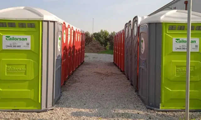 File di bagni chimici portatili, verdi e rossi, pronti per essere installati. Servizi igienici normativa rispettata.