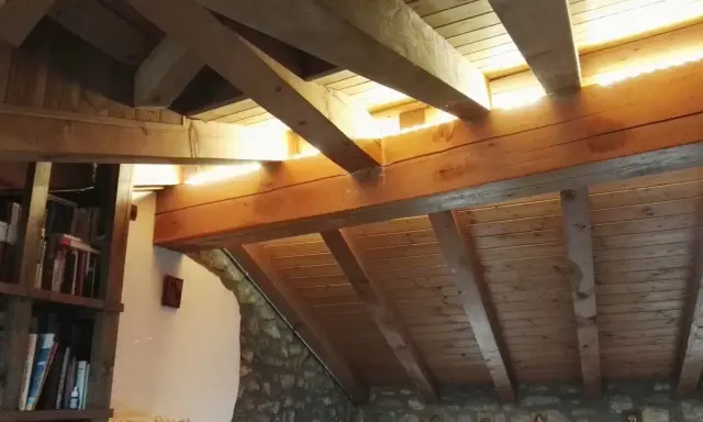 Soffitto in legno con travetti a vista, illuminato da luce naturale. Si nota una libreria e pareti in pietra. La lunghezza massima travetti solaio è ben visibile.