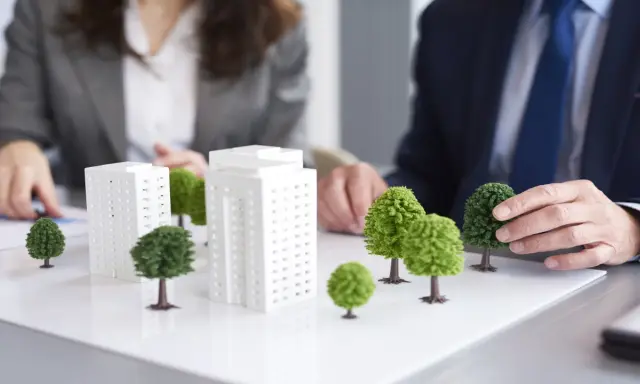 Modelli di edifici e alberi su un tavolo, che illustrano il **social housing significato** e la pianificazione urbana sostenibile.