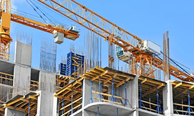 Cantiere edile con gru gialla e strutture in cemento armato. Si nota il puntellamento solaio con supporti blu e tavole di legno.