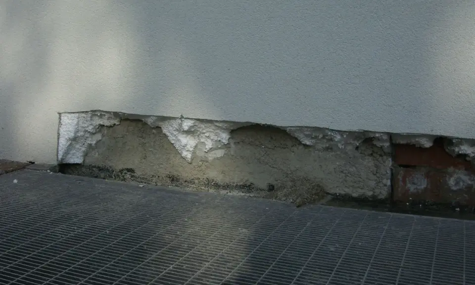 Dettaglio di un muro con isolamento danneggiato, mostrando la differenza tra xps e eps. Grata metallica in primo piano.