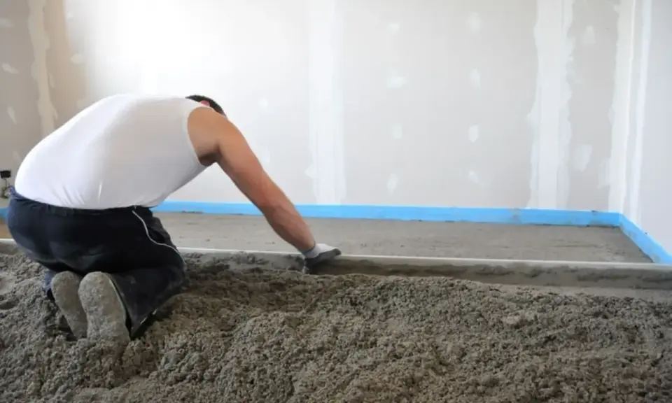 Operaio al lavoro per stendere il massetto edilizia, creando una base solida per il pavimento.