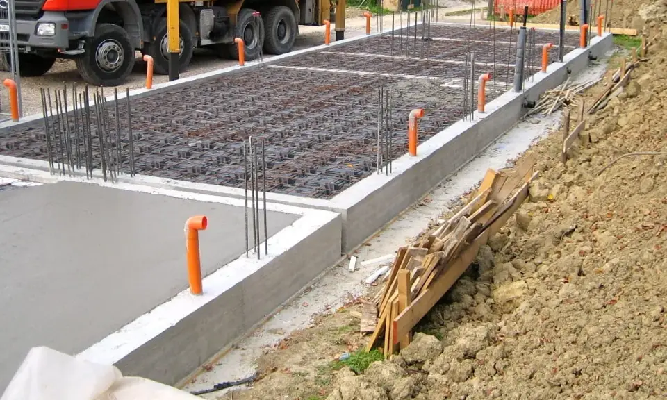 Costruzione in corso: rete di armatura e tubi arancioni per l'aerazione vespaio. Cemento fresco e un camion Beton.