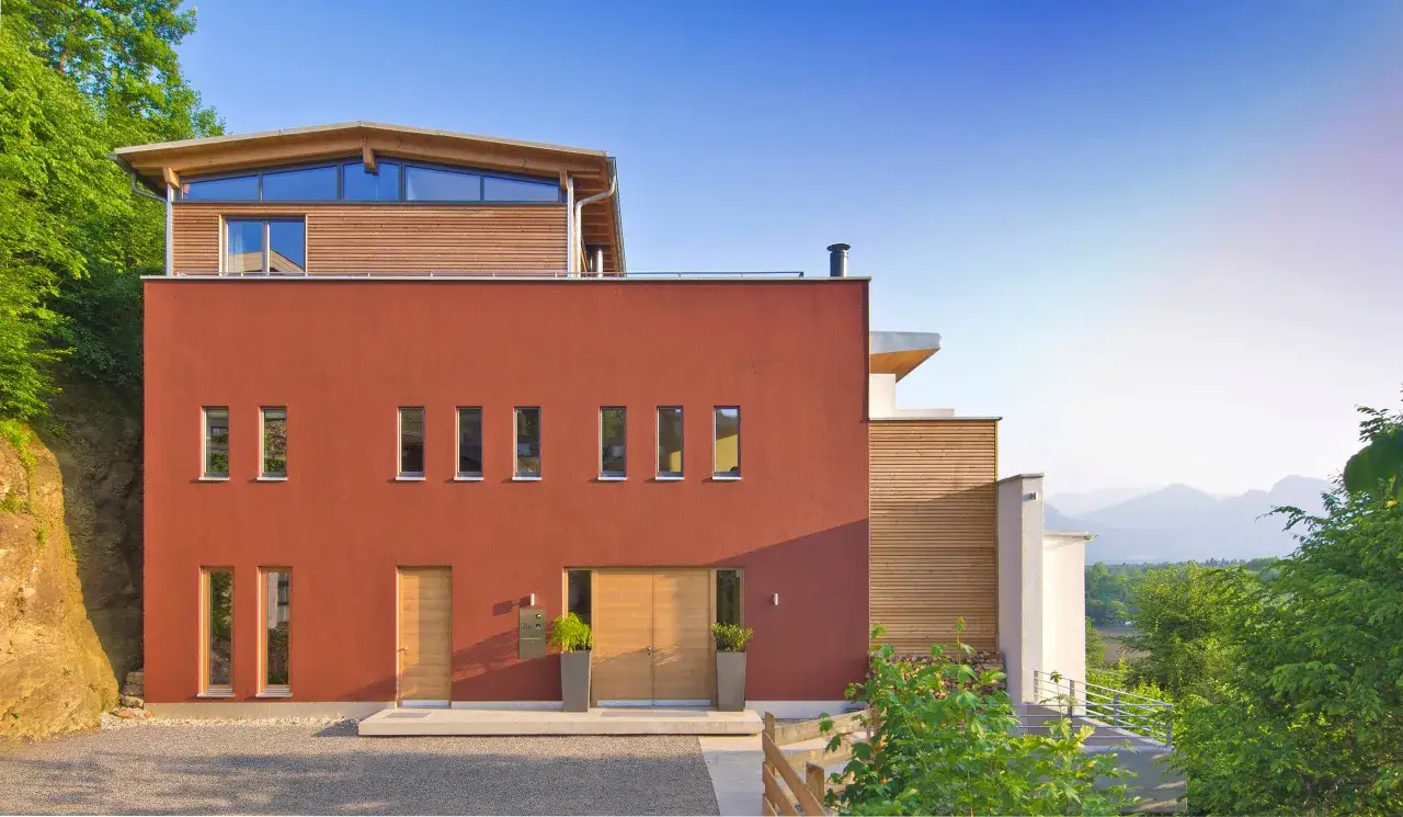 Casa moderna con colore esterno casa rosso antico, circondata da verde e montagne.