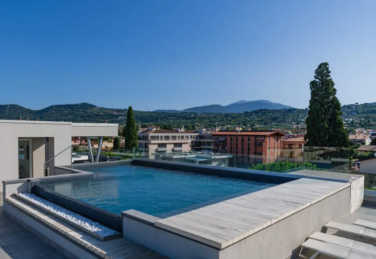 Piscina a sfioro su un terrazzo moderno, con vista panoramica su colline e case. Nessun segno di crollo, solo relax.