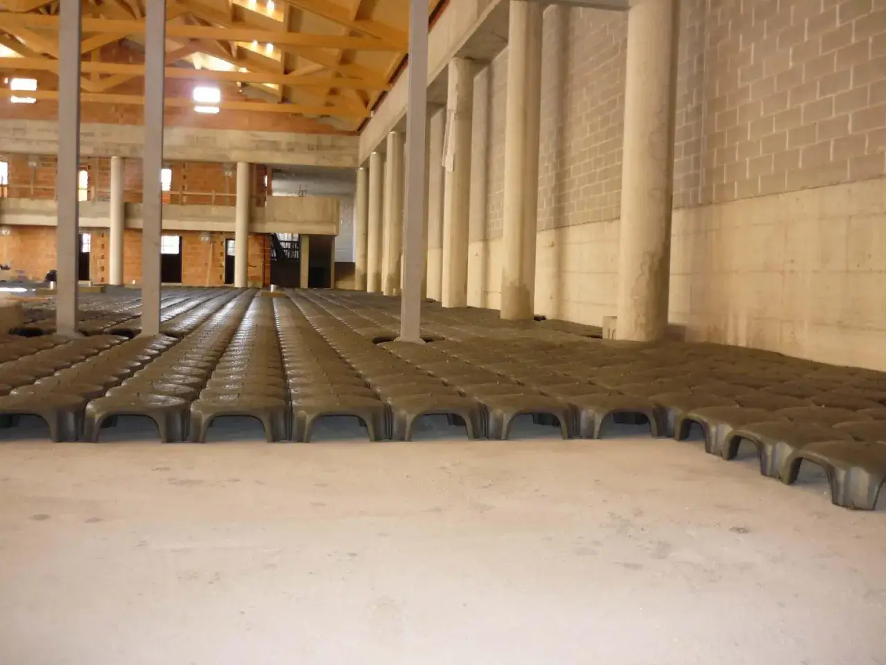 Struttura in fase di costruzione con file di elementi prefabbricati per il vespaio ghiaia. Colonne in cemento e pareti in mattoni.