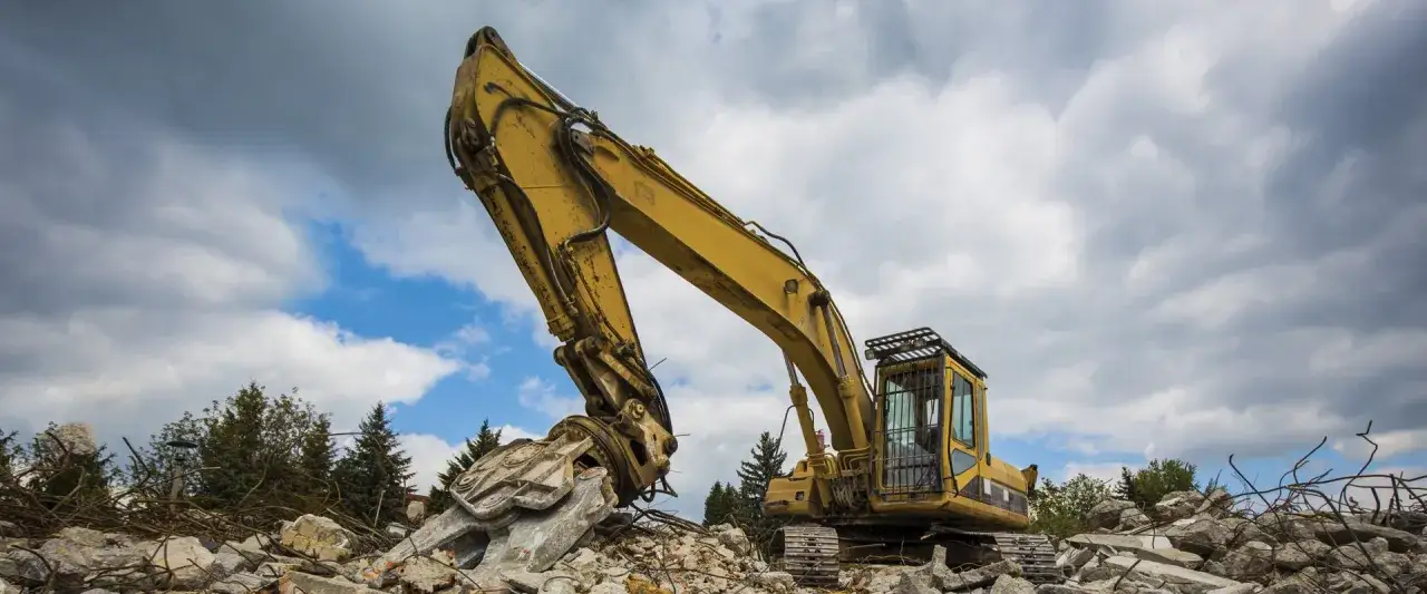 Escavatore giallo su cumuli di macerie, simbolo del materiale di risulta e della demolizione.