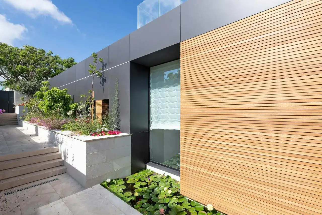 Le pareti esterne casa combinano legno e pietra, con un laghetto di ninfee e un giardino rigoglioso.