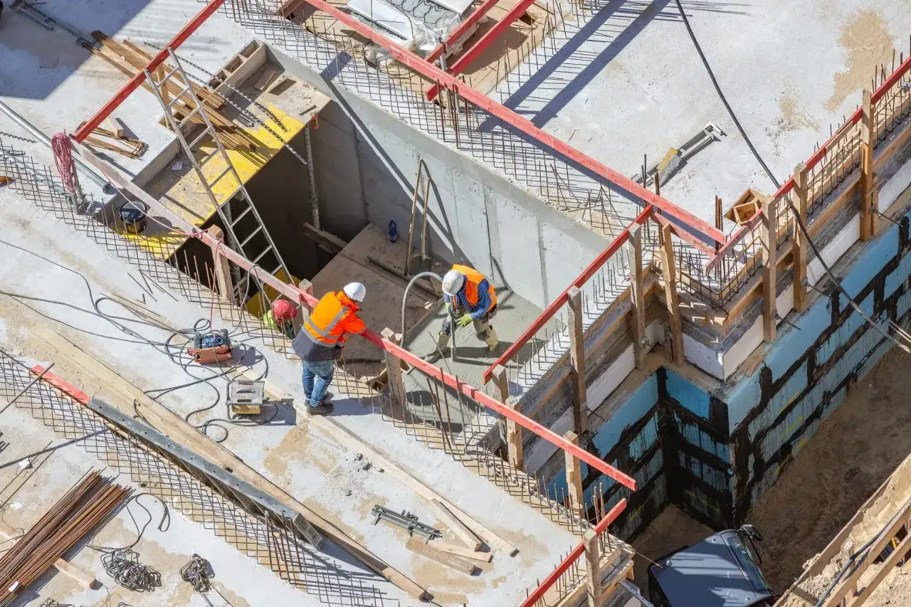 Operai in cantiere, con indumenti ad alta visibilità, lavorano alla gettata di cemento. La scena mostra la consulenza tecnica d'ufficio in azione, con attenzione ai dettagli costruttivi.