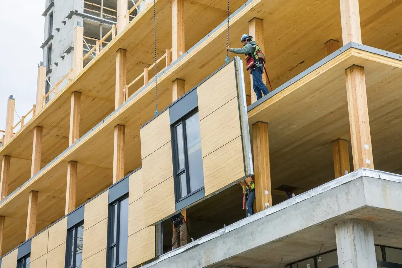Operai installano pannelli esterni su edifici in legno in costruzione. Struttura in legno a vista, con travi e pilastri.