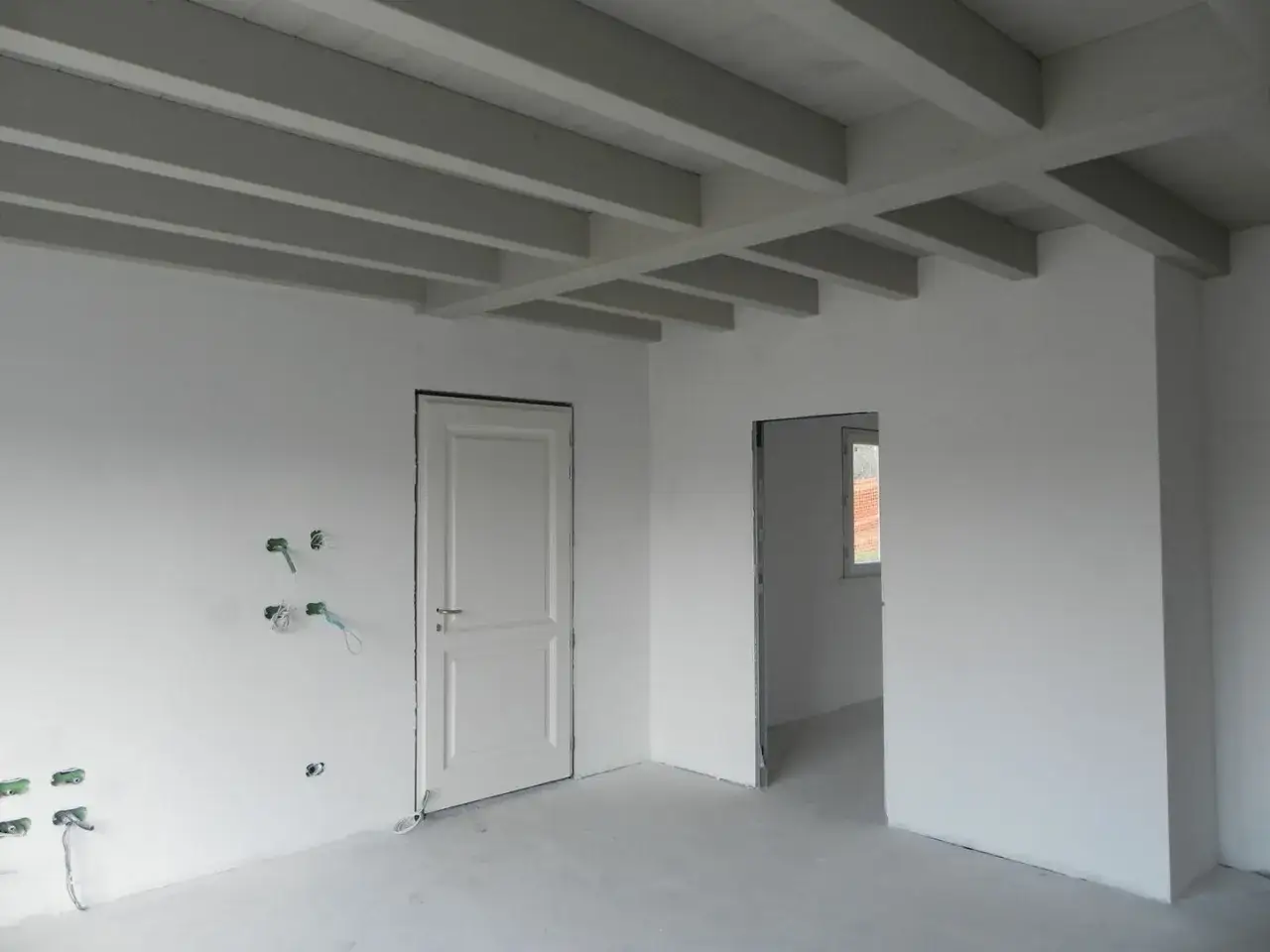 Interni in fase di finitura con intonaco civile per interni, travi a vista bianche e porte bianche.