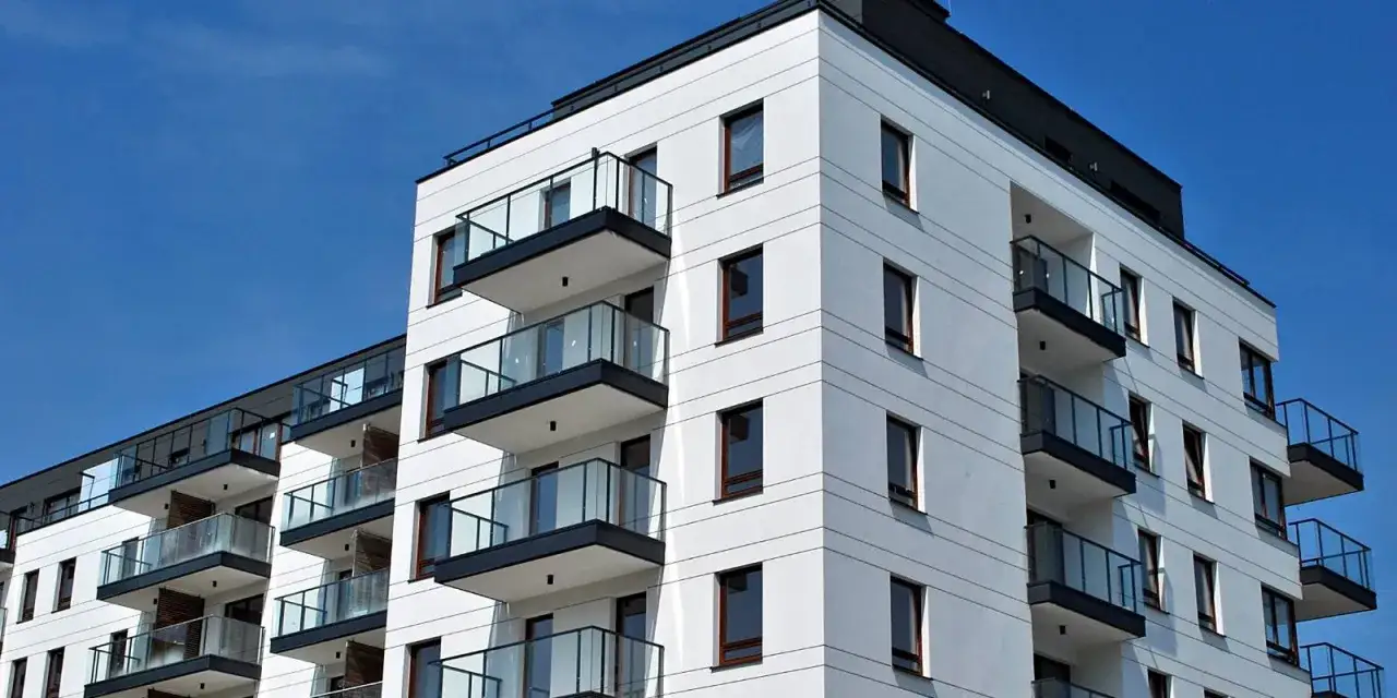 Edilizia convenzionata: pro e contro di un moderno condominio bianco con balconi vetrati sotto un cielo azzurro.