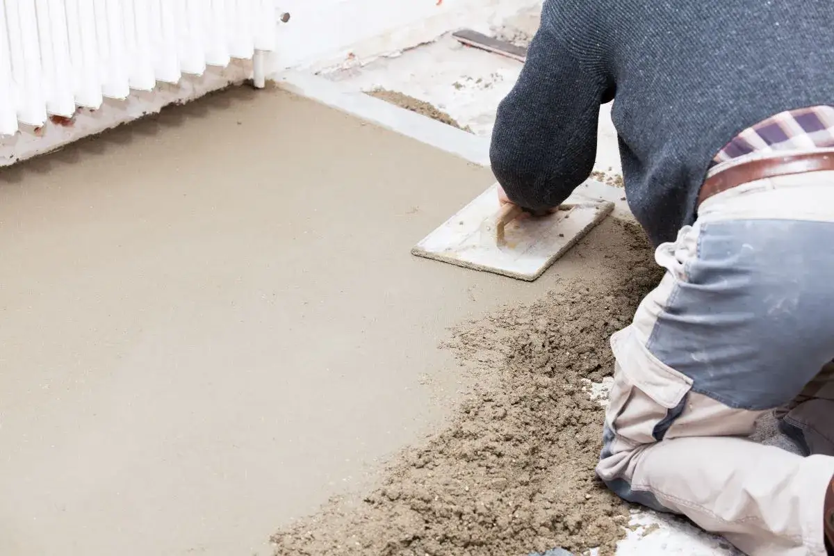 Operaio stende il massetto edilizia con una spatola, creando una base liscia per il pavimento.