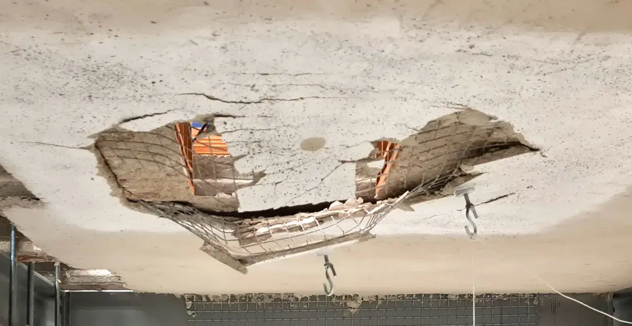 Solaio imbarcato con ampie crepe e parti mancanti, che espongono la rete metallica e i mattoni sottostanti.