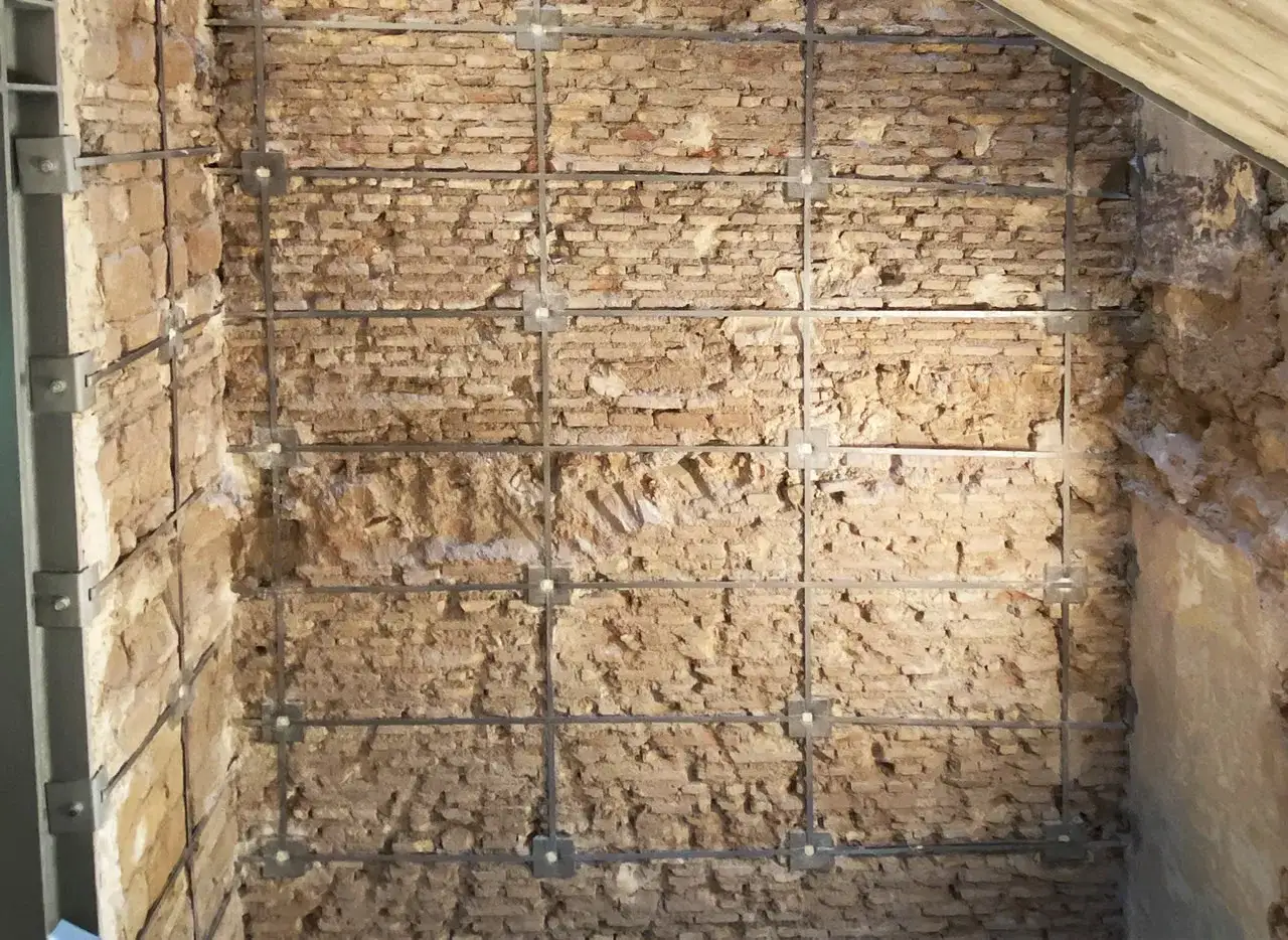 Muro in mattoni con rinforzi metallici a griglia, parte di un intervento locale di consolidamento.