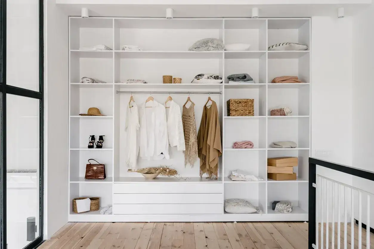Armadio a muro bianco con abiti appesi, cappelli, borse e cesti. Un esempio di come organizzare un armadio a muro in modo ordinato ed elegante.