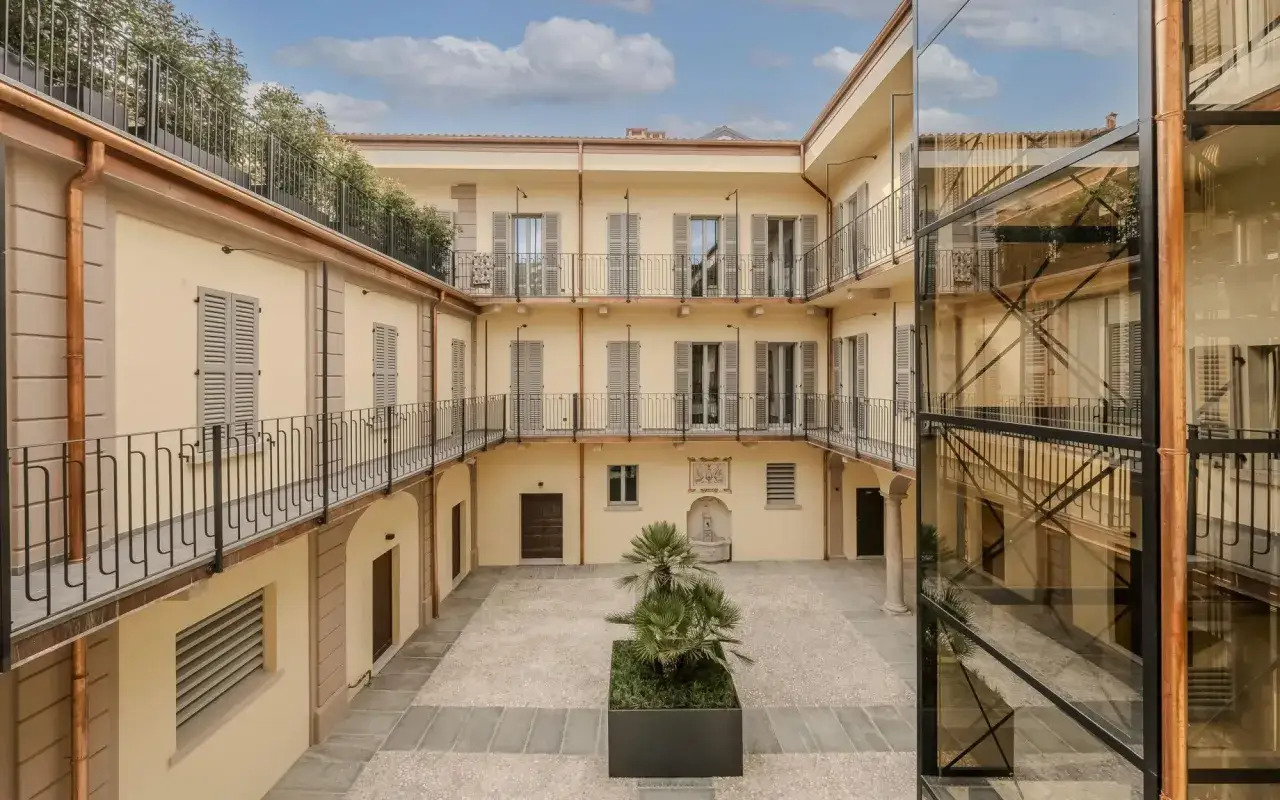 Cortile interno di un edificio con balconi e un ascensore moderno in vetro. Un esempio di come l'edilizia popolare possa integrarsi con elementi contemporanei.