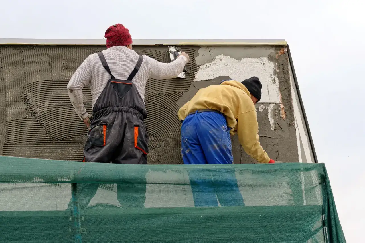 Operai applicano intonaco su un muro, creando diversi tipi di rasatura con spatole.