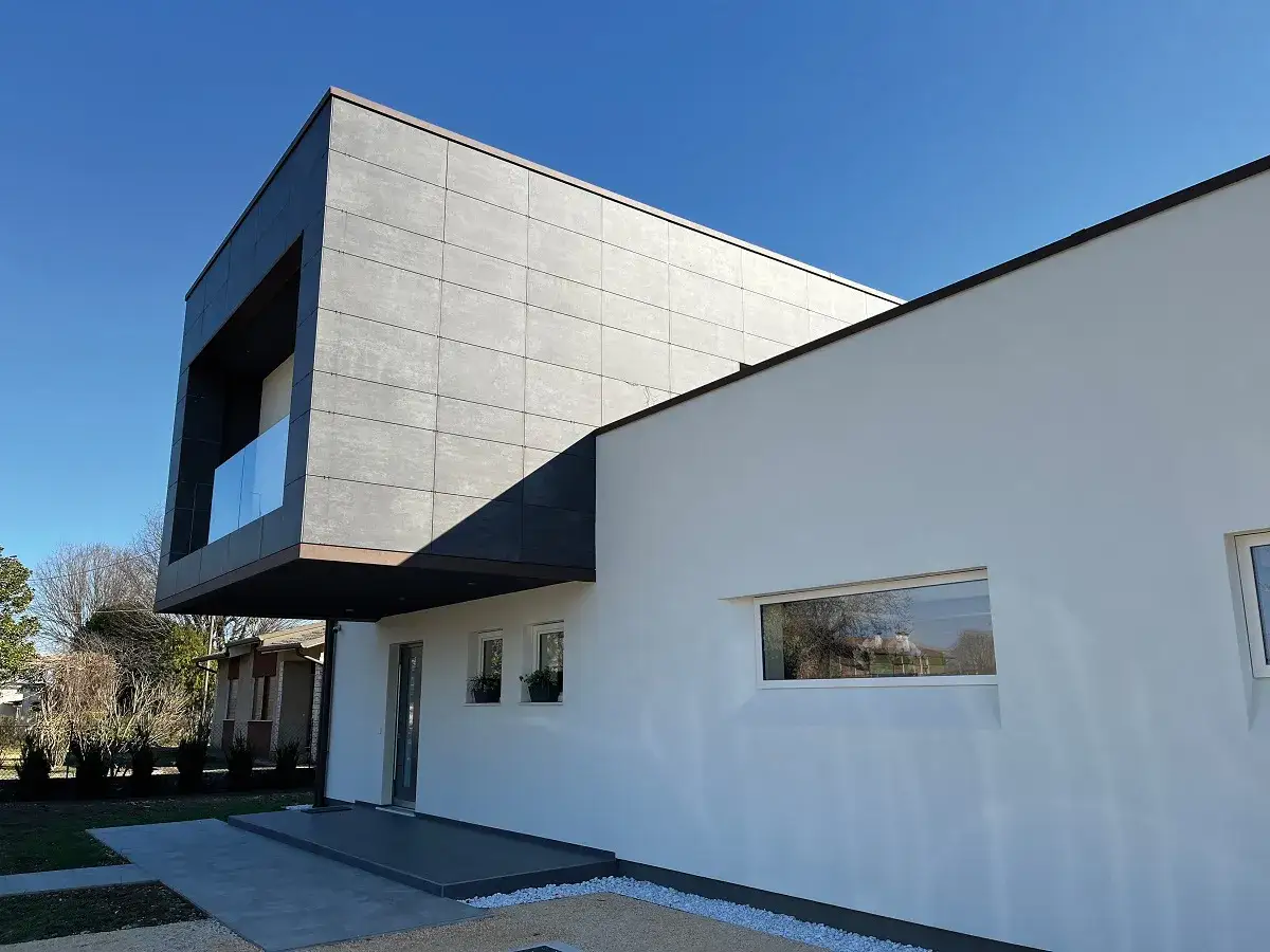 Moderna abitazione con una facciata ventilata in grigio scuro e bianco, con ampie finestre e un balcone in vetro.