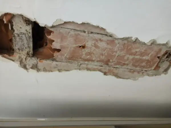 Intonaco danneggiato rivela l'intradosso del solaio con mattoni a vista e travi in legno.